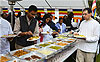 People serving food at outdoor buffet event.